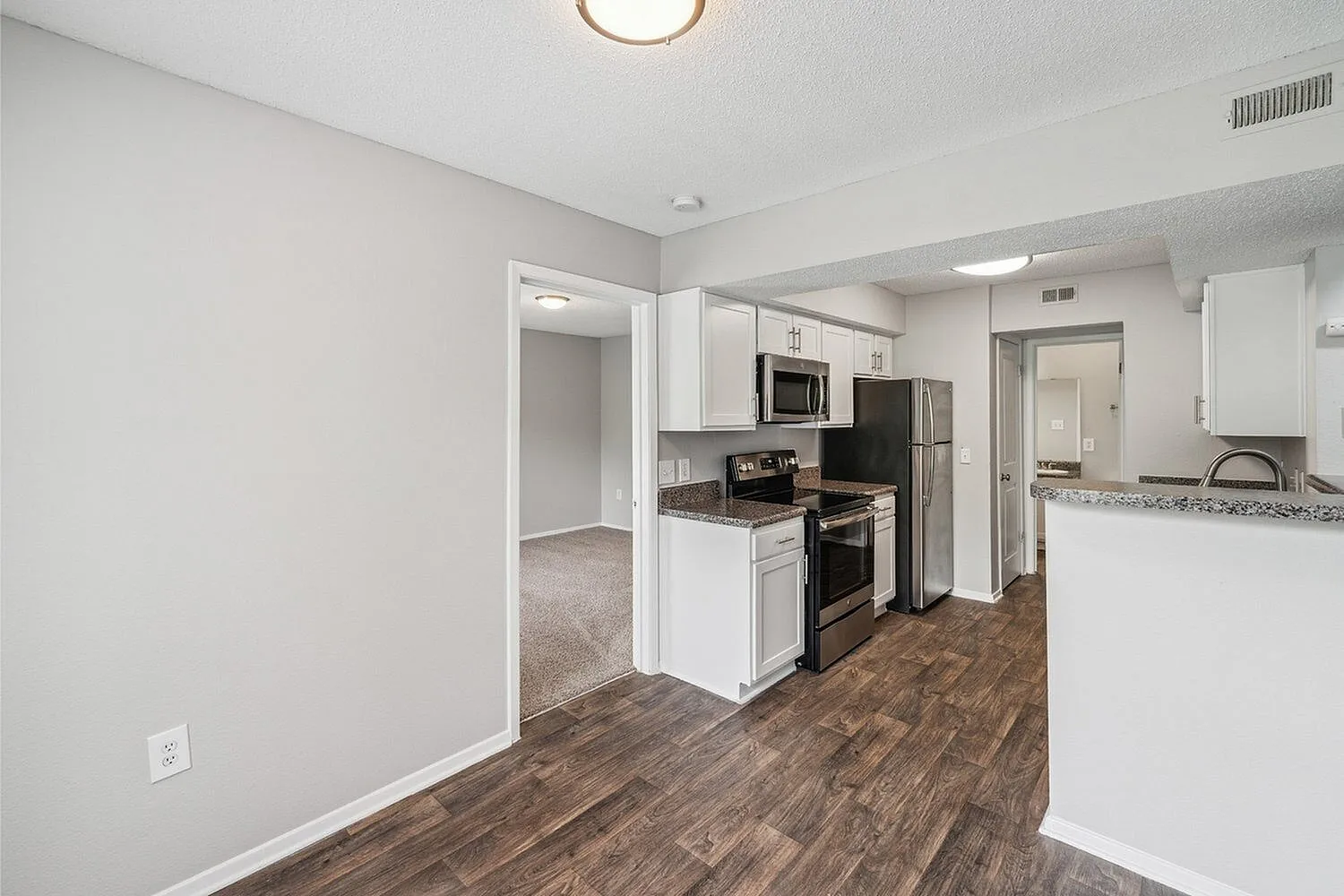 Modern kitchen with sleek stainless steel appliances, rich wood flooring, and open entryway leading to a cozy carpeted room.
