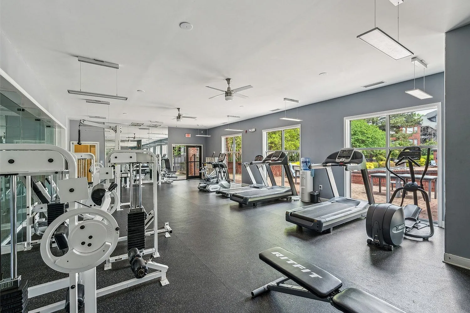 Modern apartment fitness center with state-of-the-art gym equipment, treadmills, and large windows offering scenic views.