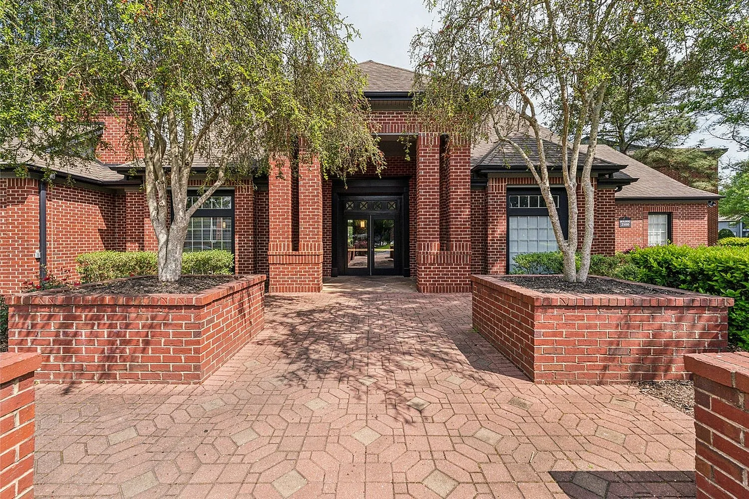 Charming brick apartment entrance framed by lush trees, offering a welcoming and elegant ambiance.