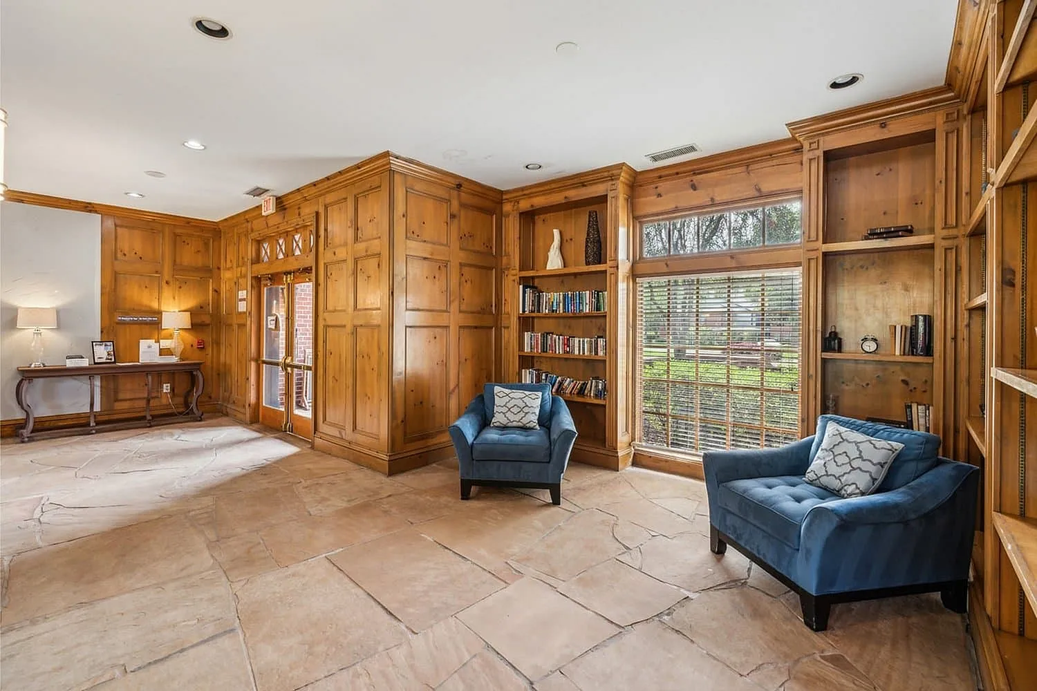 Inviting reading nook with elegant wooden paneling, cozy blue armchairs, and ample natural light streaming through large windows.