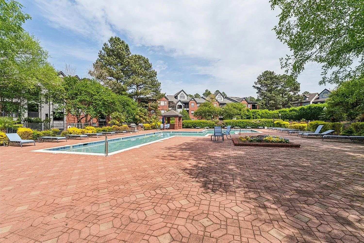 Inviting outdoor swimming pool area with lounge chairs, surrounded by lush greenery and charming residential buildings.