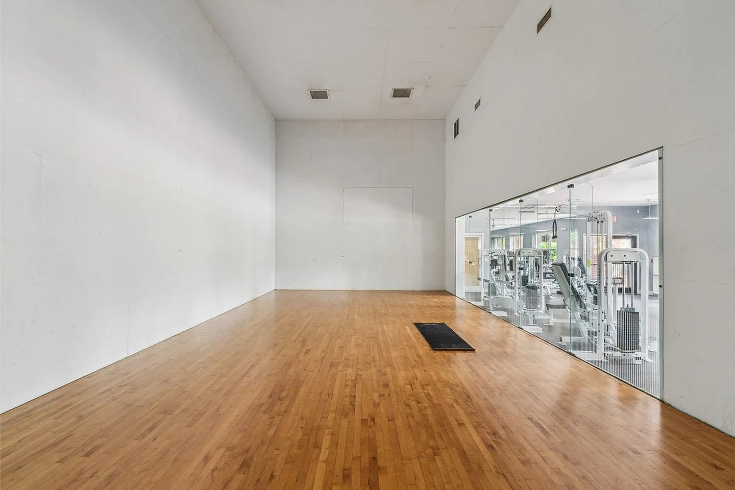 Spacious fitness room with wooden floors and a glass wall revealing state-of-the-art gym equipment, perfect for active lifestyles.