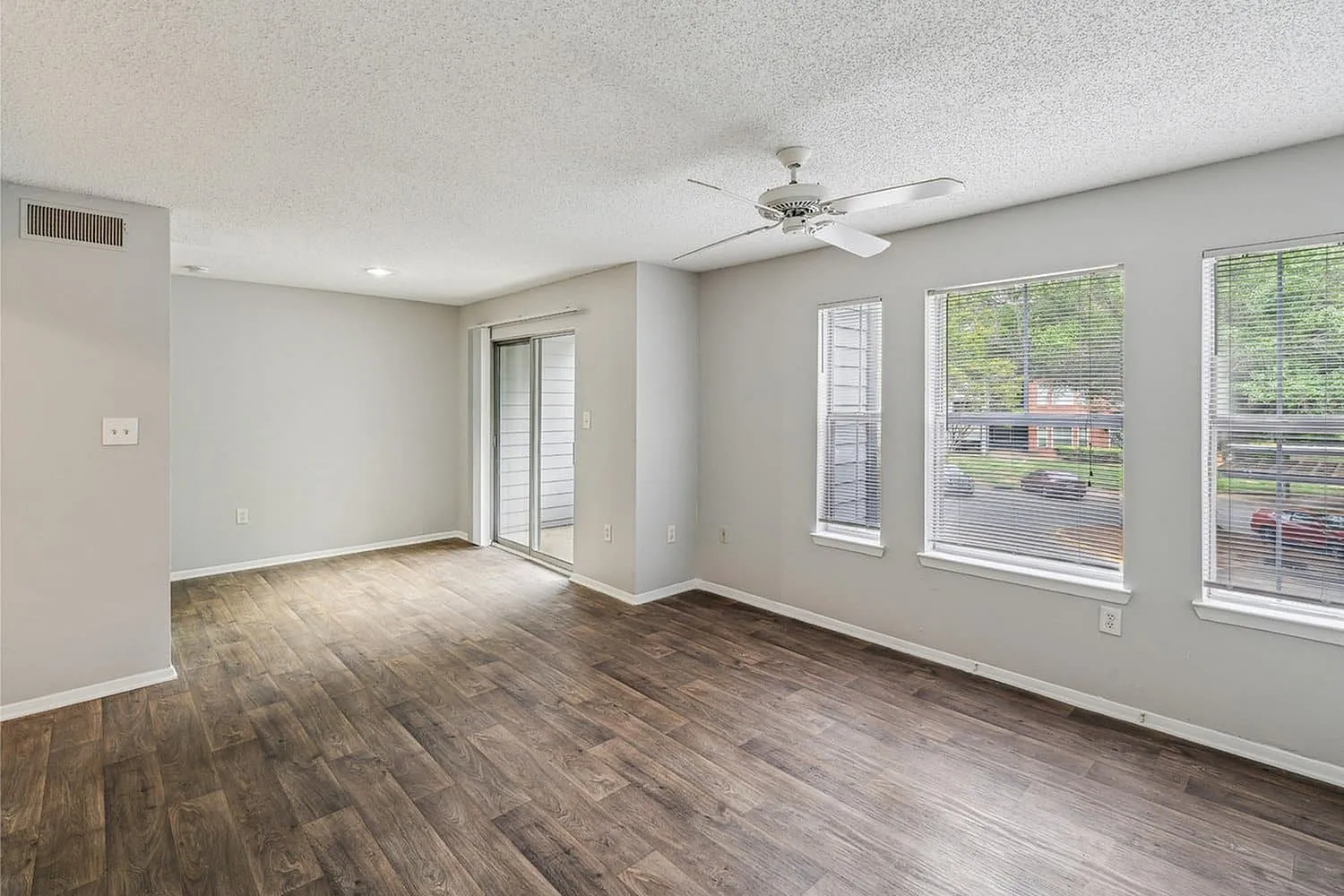 Bright and airy living room with large windows, elegant wood flooring, and modern ceiling fan, ideal for a relaxing atmosphere.