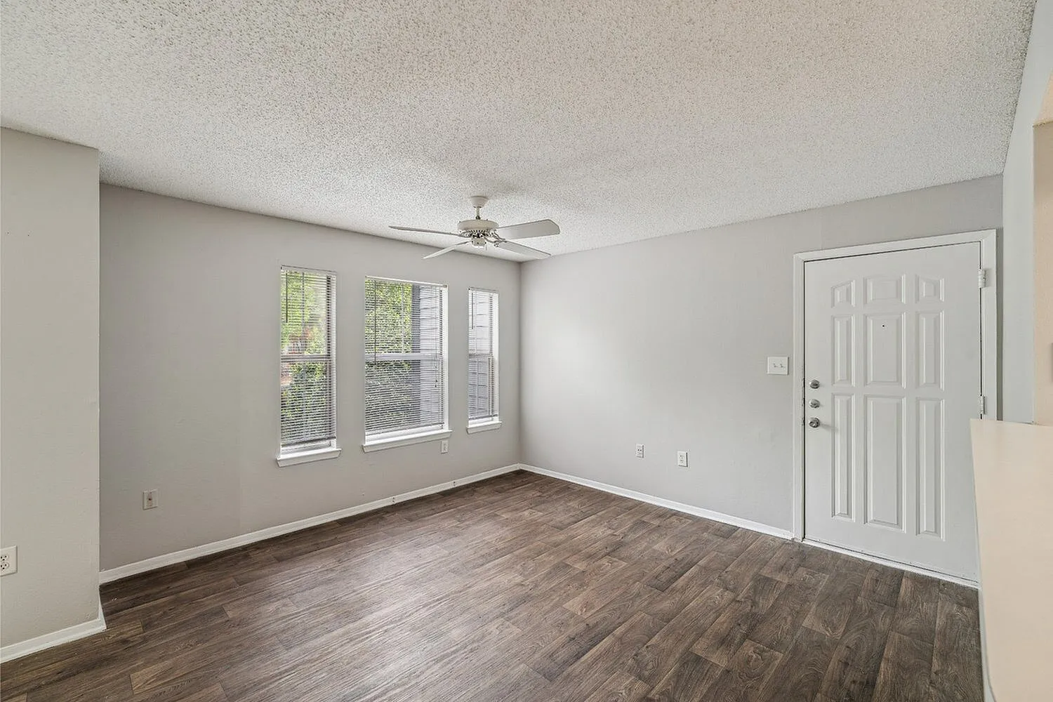 Bright and airy apartment room with stylish wooden flooring, large windows for natural light, and a modern ceiling fan.