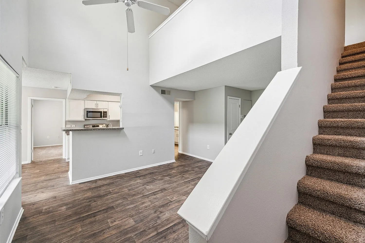 Bright and spacious living area with elegant wood flooring, open kitchen concept, and plush carpeted staircase leading to the upper level.