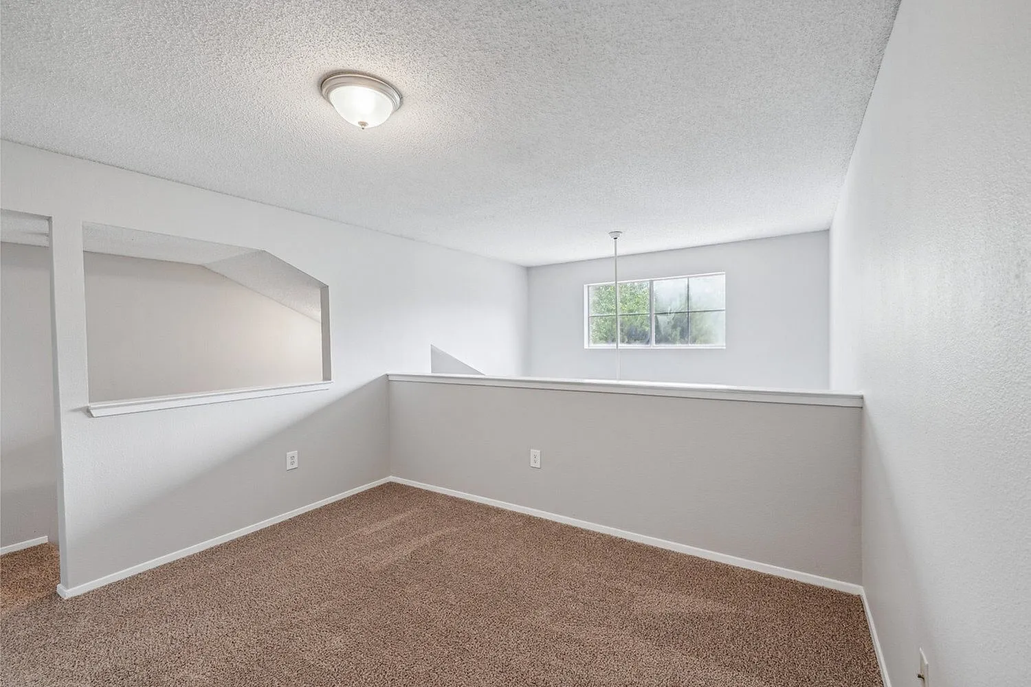 Bright and airy loft space with plush carpeting and a large window, perfect for a cozy retreat.