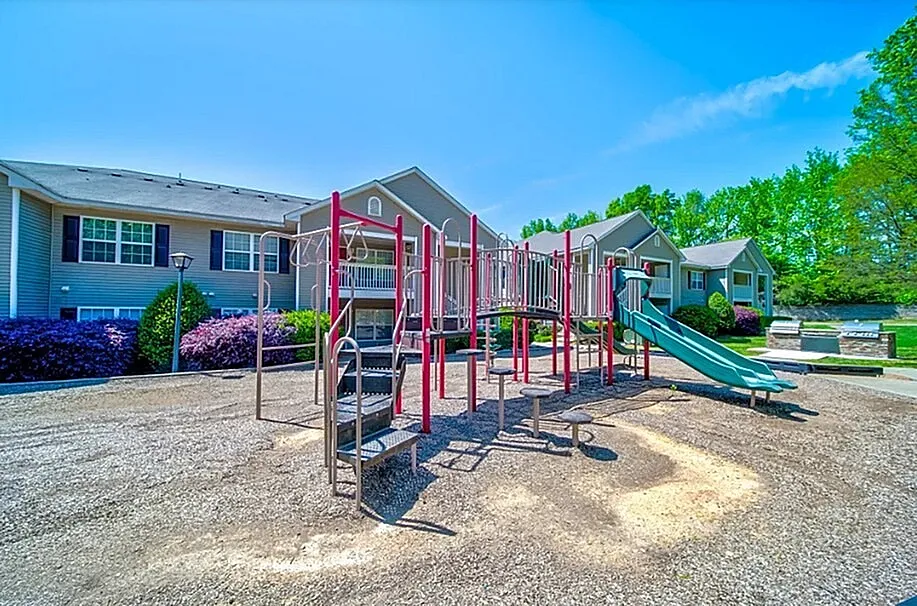 Charming apartment complex with vibrant playground surrounded by lush greenery, perfect for family living.