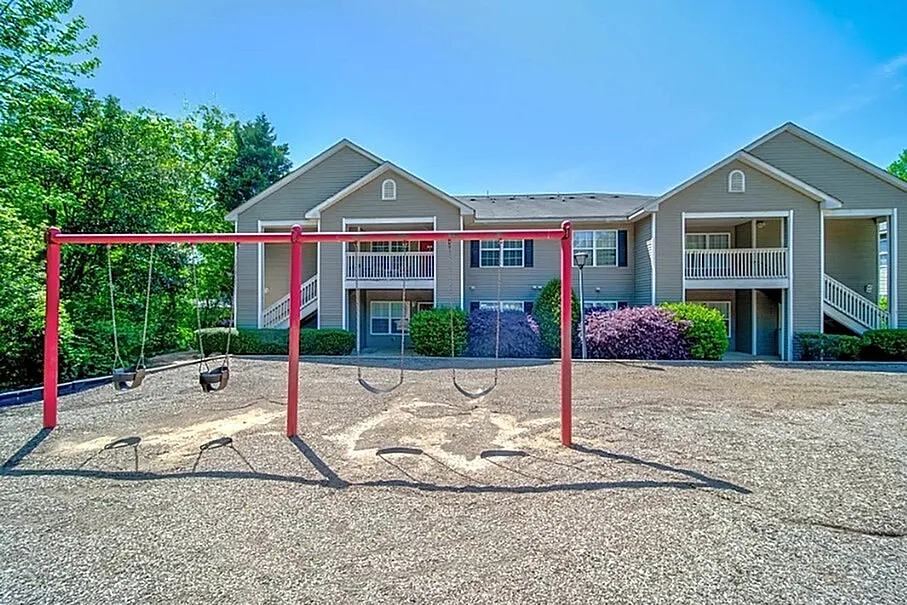 Charming apartment building with inviting balconies surrounded by lush greenery and a colorful playground in front.