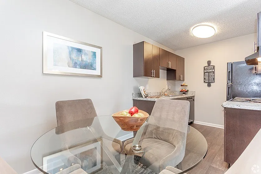 Chic dining area with a glass table, cozy chairs, and modern kitchen in a stylish apartment.