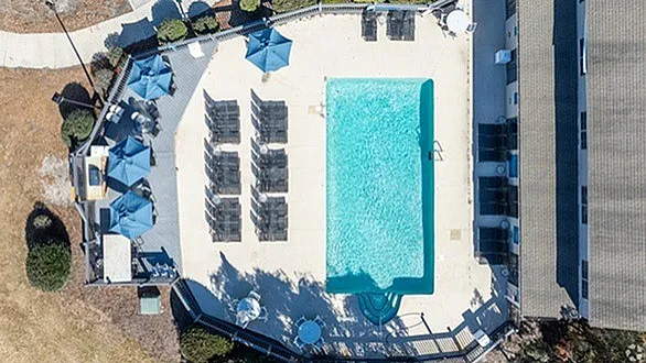 Inviting aerial view of a luxurious pool area with sun loungers, shaded seating, and lush surroundings, perfect for relaxation.