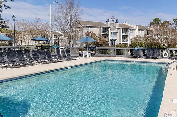 Inviting apartment complex with a crystal-clear swimming pool, surrounded by modern buildings and lush greenery, offering a perfect blend of relaxation and contemporary living.