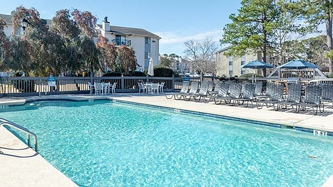 Inviting apartment complex with crystal-clear swimming pool, surrounded by sun loungers and umbrellas for a perfect relaxation spot.