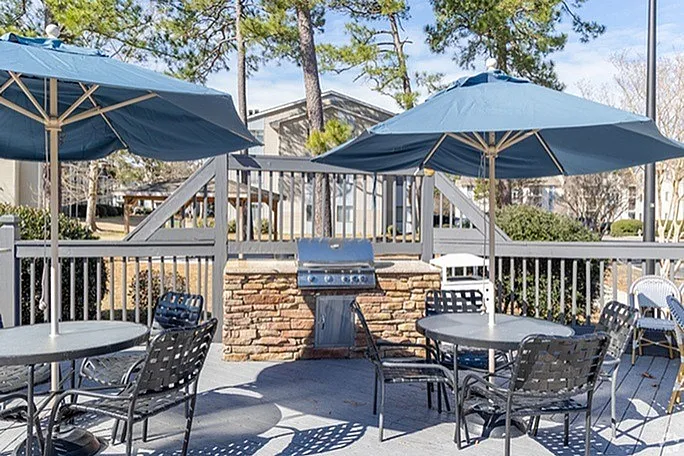 Charming outdoor patio with stylish furniture, large blue umbrellas, and a modern grill, perfect for entertaining.