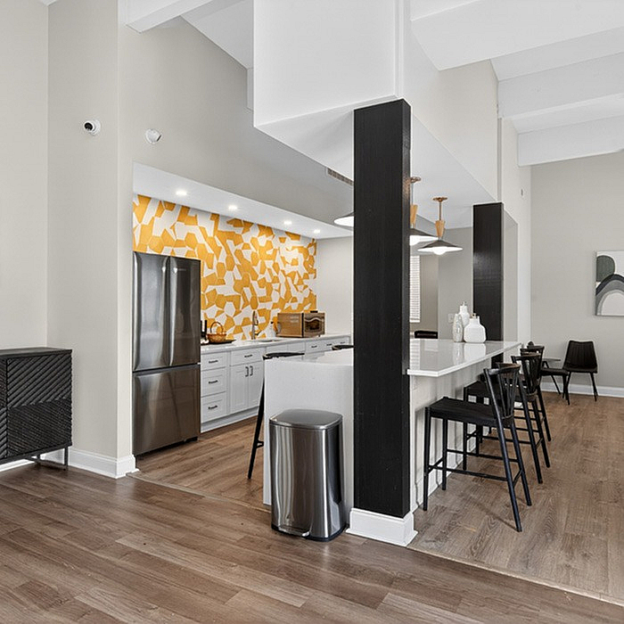 Modern and inviting kitchen area with a vibrant yellow mosaic backsplash, sleek stainless steel appliances, and a stylish breakfast bar with chic black seating.