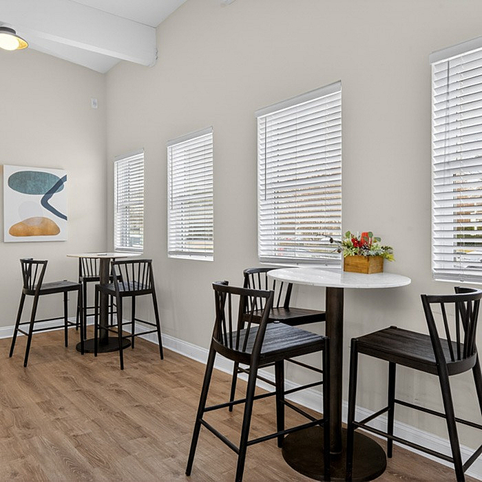 Bright and airy residential dining area with modern high-top tables, stylish artwork, and natural light streaming through large windows.