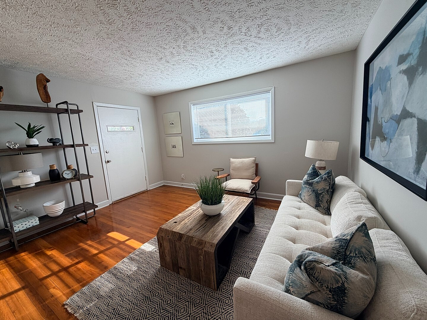 Bright and inviting living room with modern decor, featuring a cozy sofa, stylish wooden coffee table, and elegant shelving on pristine hardwood floors.
