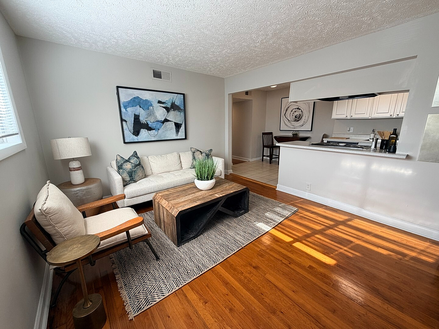 Charming open-concept living room with sleek wood flooring, modern decor, and natural light, seamlessly connected to a stylish kitchen.