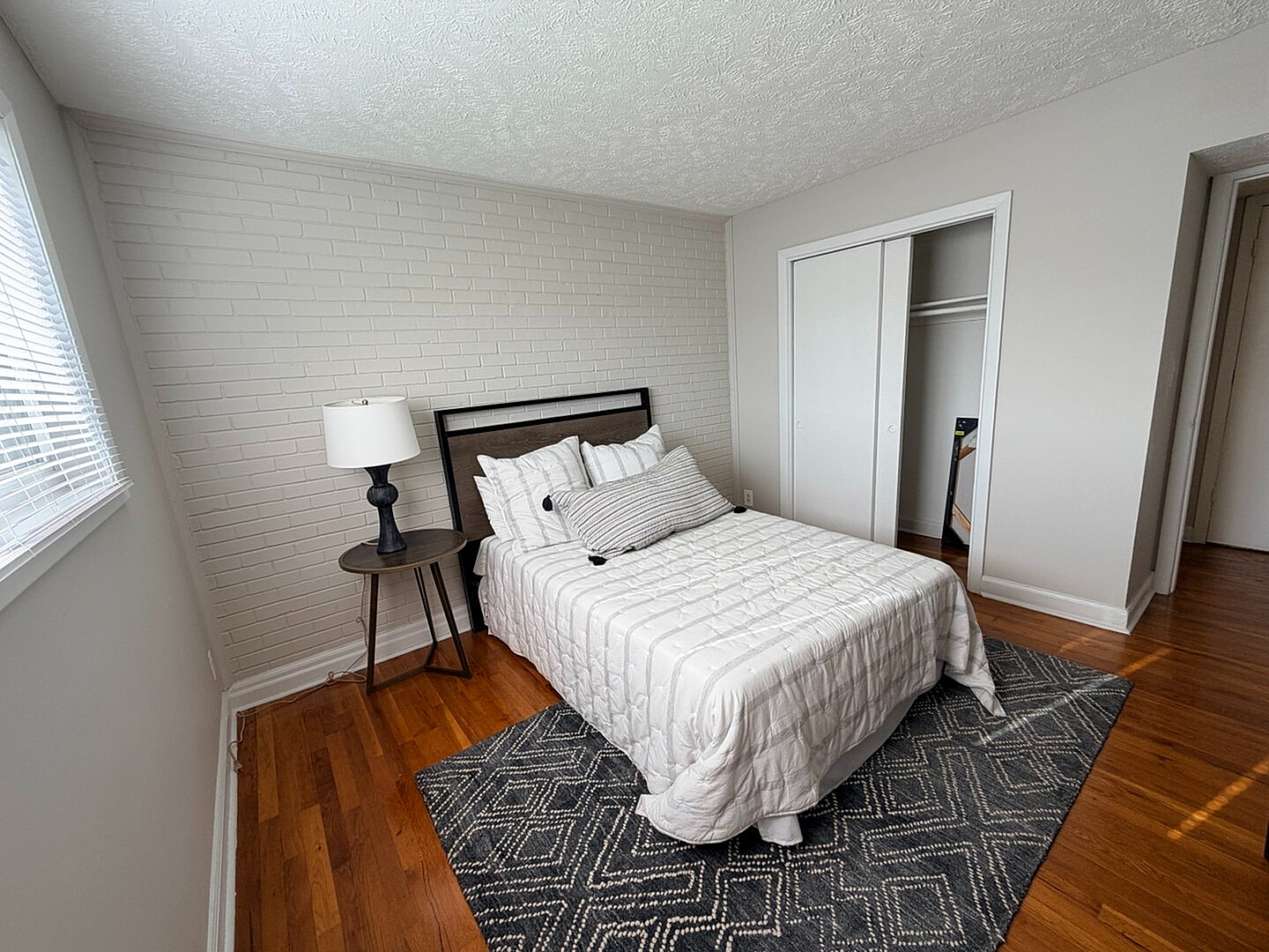 Bright and cozy bedroom featuring a comfortable bed, modern bedside table with lamp, and elegant hardwood flooring, perfect for a peaceful retreat.