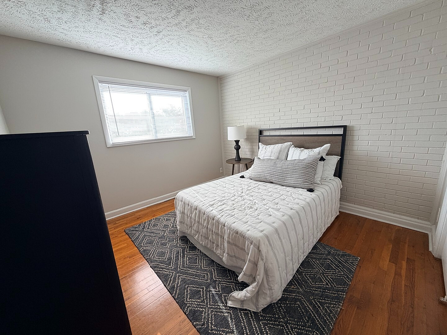Inviting bedroom with elegant brick accent wall, cozy bedding, and abundant natural light.