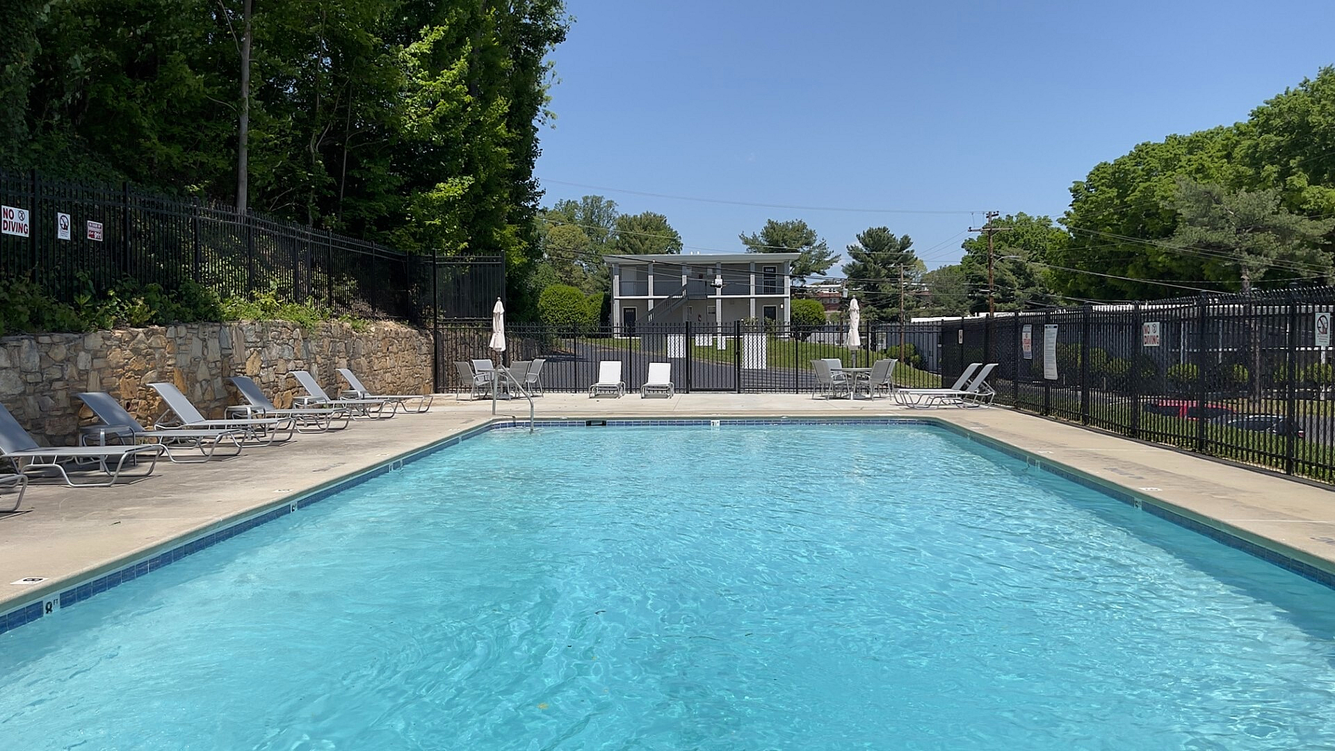 Inviting apartment complex with a sparkling outdoor pool surrounded by lounge chairs, offering a perfect relaxation spot under clear blue skies.