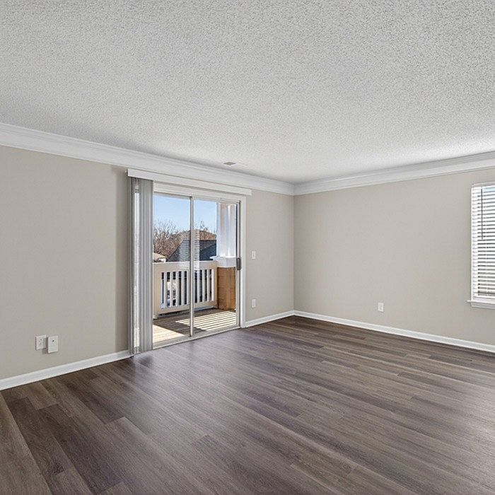 Bright and spacious living room with elegant wood flooring, featuring a large window and a sliding glass door opening to a charming balcony.