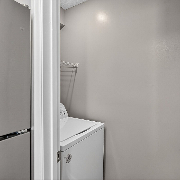 Compact laundry nook featuring a modern washing machine with convenient storage shelf above.