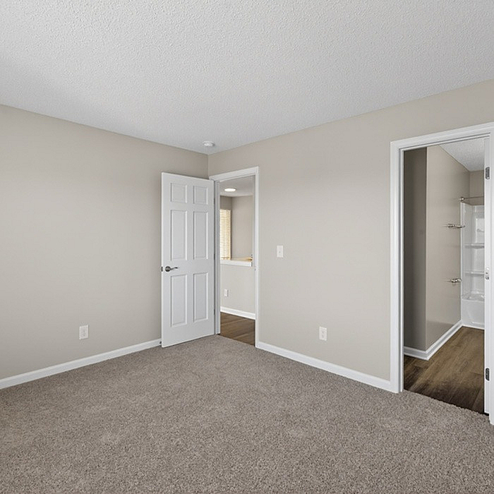 Bright and airy bedroom with plush carpeting and neutral tones, connected to a sleek bathroom, offering modern comfort and style.