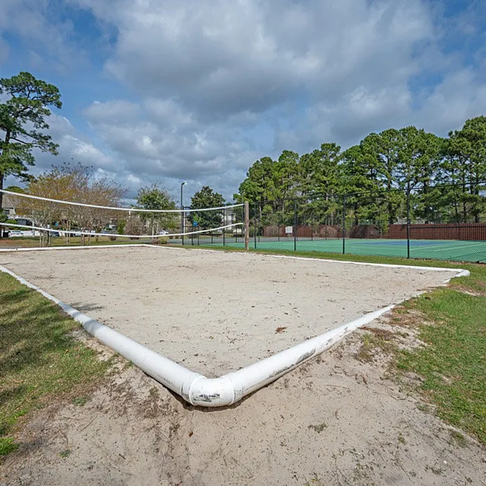 Inviting outdoor sand volleyball court surrounded by lush greenery and blue skies, perfect for recreation and relaxation.
