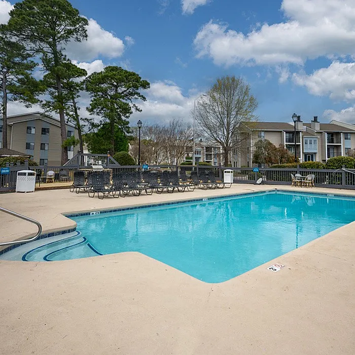 Inviting outdoor pool surrounded by lush greenery and elegant apartment buildings under a clear blue sky.