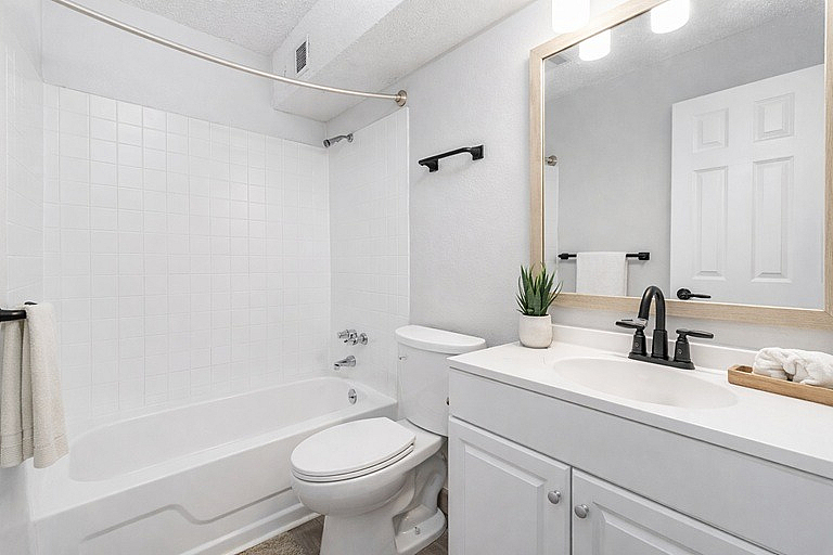 Bright, modern bathroom with elegant fixtures, featuring a pristine bathtub, chic white vanity, and stylish decor.