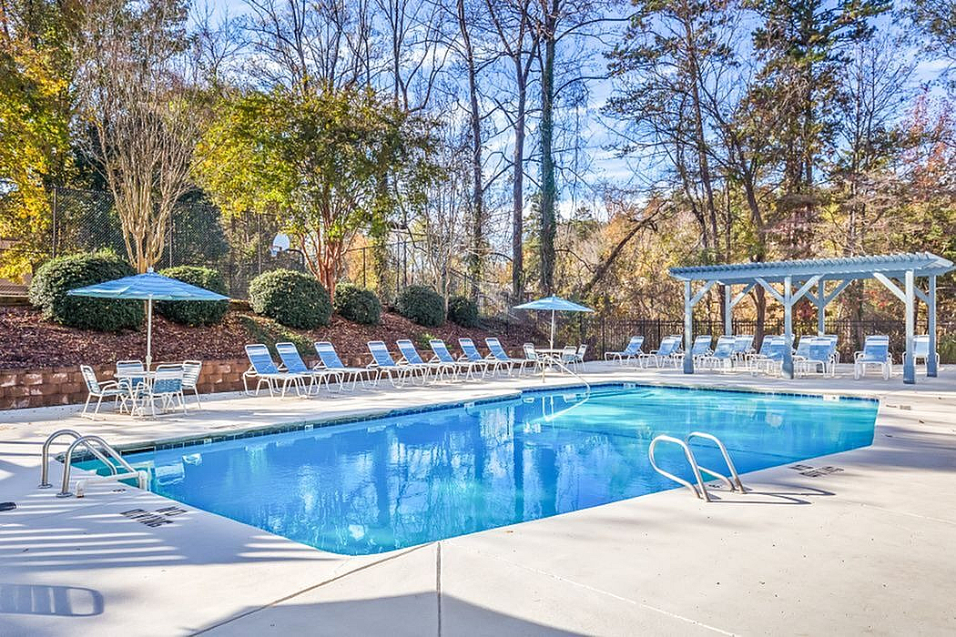 Inviting outdoor pool area with plentiful seating, surrounded by lush trees creating a serene retreat.