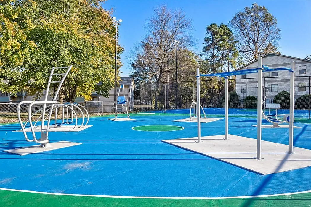 Vibrant outdoor fitness park with modern exercise equipment, surrounded by lush greenery and blue courts.