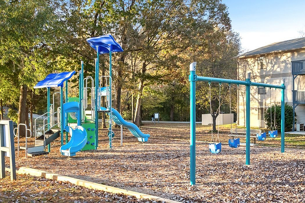 Inviting playground with vibrant blue slides and swings set among lush trees, offering a perfect family-friendly outdoor space.