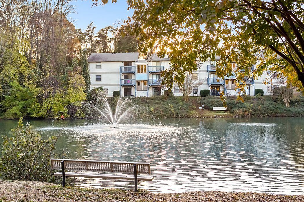 Charming apartment complex with serene lake view, picturesque fountain, and lush greenery, perfect for relaxation and tranquility.