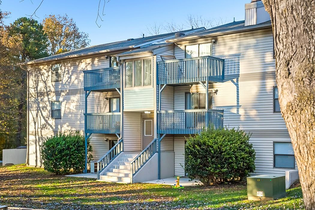 Charming multi-story apartment building with inviting blue balconies and lush green surroundings under a clear sky.