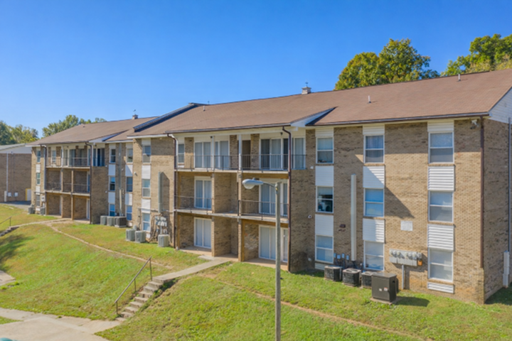 Charming three-story brick apartment complex with inviting balconies, nestled in a lush green setting, offering a serene and welcoming living environment.