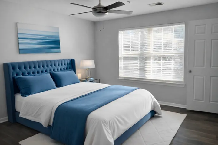 Elegant bedroom with a plush blue bed, chic artwork, and abundant natural light through large windows.
