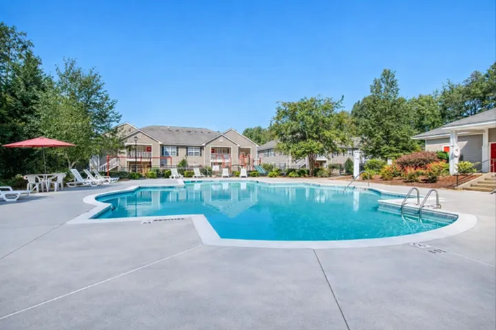 Inviting apartment complex showcasing a serene swimming pool surrounded by lush greenery, perfect for relaxation.