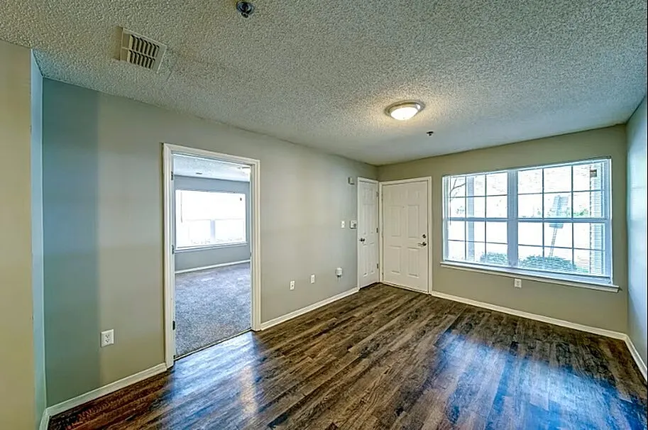 Bright and inviting living space with large windows and elegant hardwood flooring, leading into a cozy carpeted room.