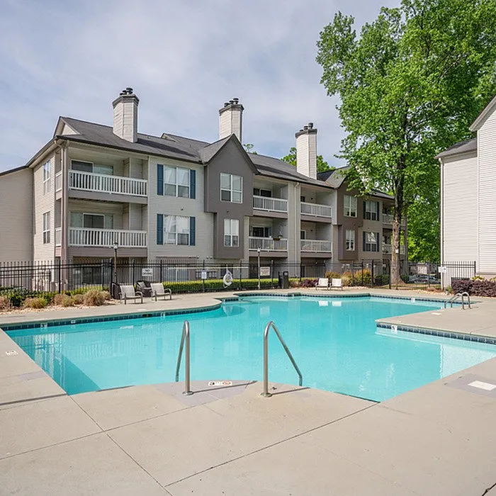 Serene apartment complex with a sparkling blue swimming pool, surrounded by lush greenery and modern balconies.