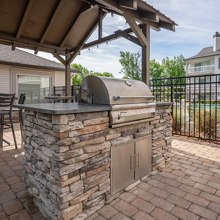 Charming outdoor BBQ area with a sleek stone grill under a cozy covered patio, perfect for entertaining.