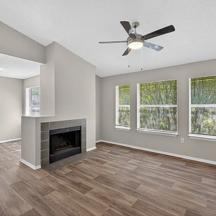 Charming living area with large windows, a modern ceiling fan, and a stylish fireplace, perfect for cozy relaxation.