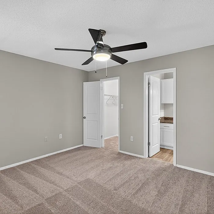 Inviting bedroom with plush carpet, modern ceiling fan, and walk-in closet, perfect for serene living.