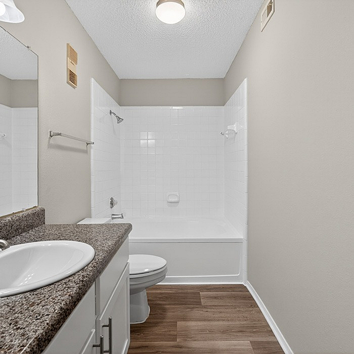 Bright and modern bathroom featuring sleek granite countertops, a spacious mirror, and elegant tile bathtub with soft lighting.