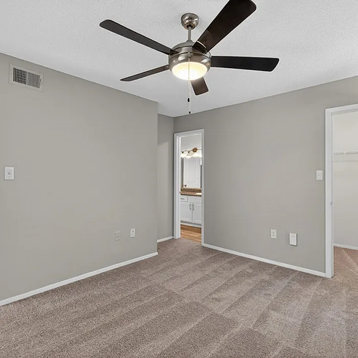 Inviting bedroom with plush carpet, modern ceiling fan, and a view into a stylish en-suite bathroom.