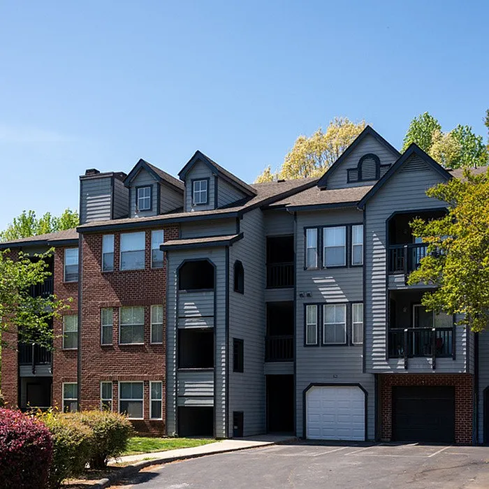Charming apartment exterior with modern architecture, brick and siding facade, and lush green surroundings under a clear blue sky.