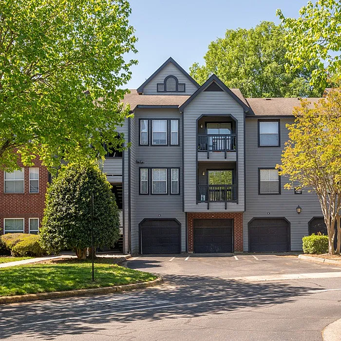 Charming multi-story apartment complex with modern design, surrounded by lush greenery and ample parking space.