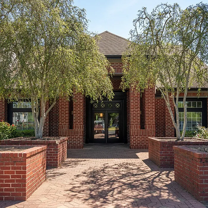 Charming brick building entrance with lush greenery and welcoming atmosphere.