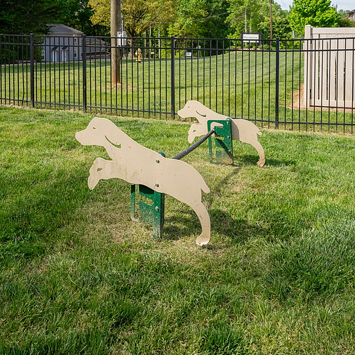 Charming outdoor dog park with playful dog-shaped hurdles on lush green grass, perfect for pet-friendly living.