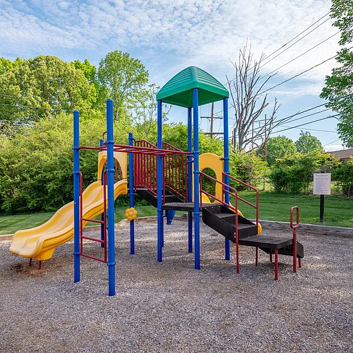 Inviting outdoor playground with vibrant slides and climbing structure, set against lush greenery and a clear blue sky.